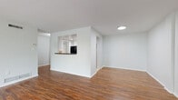 This single-floor residence offers a clean, functional layout with a cohesive design throughout. The open living area is anchored by warm, rich hardwood-style flooring that extends across the main living spaces, complemented by crisp white walls and neutral tones that create a bright, welcoming atmosphere.

The kitchen is defined by a distinctive pass-through window opening onto the living area, promoting an open and connected feel. It features white cabinetry, dark granite countertops, a tile backsplash with a decorative mosaic accent band, and black appliances including a gas range, refrigerator, and built-in microwave. The kitchen floor transitions to light tile, adding a practical touch to the cooking space.

The bedrooms are carpeted in soft neutral tones and feature large windows that invite generous natural light and offer views of surrounding greenery, creating a calm and comfortable retreat. The layout also accommodates a dedicated dining or flex area adjacent to the kitchen.

The bathroom is finished with beige ceramic tile flooring and tub surround, accented by a mosaic tile border, and includes a rich wood-toned vanity with granite countertop. A separate shower with glass sliding doors and matching tile finishes adds a refined touch. Overall, the space presents a tidy, move-in-ready environment with consistent finishes throughout.