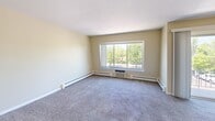 Located at 241 Ottawa Bend Drive in Morris, Illinois, this single-floor residence offers a well-organized layout across two bedrooms, one bathroom, and a combined kitchen and living area. The open living room features soft carpeting, neutral beige walls, and a large picture window that frames outdoor tree views and fills the space with natural light. Baseboard heating runs along the perimeter, ensuring efficient warmth throughout. The kitchen is appointed with warm-toned wood cabinetry, dark countertops, a stainless steel sink set into a peninsula, and white appliances including a gas range and refrigerator. Both bedrooms are carpeted and feature ceiling fans with integrated lighting. The primary bedroom is generously proportioned, offering a built-in closet and natural light from a window overlooking the greenery outside. The second bedroom also includes a ceiling fan and closet storage, providing a comfortable and functional space. The full bathroom includes a walk-in shower with built-in shelving, a wood-vanity with sink, and tile flooring. Throughout the residence, clean white trim and neutral tones create a cohesive, understated aesthetic that offers a versatile backdrop for a variety of interior styles.