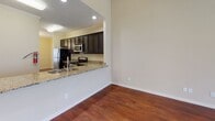 This single-floor residence offers a thoughtfully designed layout that balances open living spaces with comfortable private areas. Rich, dark hardwood flooring flows throughout the main living and kitchen areas, lending warmth and a sense of continuity to the interior.

The living room is a standout feature, boasting soaring vaulted ceilings, recessed lighting, and a ceiling fan. French doors and an adjacent window flood the room with natural light while providing direct access to the outdoors. The open-concept kitchen connects seamlessly to the living area via a pass-through granite countertop breakfast bar. Dark espresso cabinetry, stainless steel appliances — including a range, microwave, and refrigerator — and granite countertops give the kitchen a modern, functional character.

A hallway lined with crisp white paneled doors and crown molding leads to the bedrooms and bathrooms. The bedrooms feature plush carpet, vaulted or standard ceilings, and windows with blinds that invite natural light while maintaining privacy. Both bathrooms are finished with tile flooring, dark vanity cabinetry, light stone countertops, and a tub-shower combination with a curved curtain rod. Warm, neutral wall tones throughout the home create a cohesive and inviting ambiance.