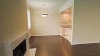 This single-floor residence offers a well-designed open layout that seamlessly connects the main living and dining areas. Rich, dark hardwood flooring runs throughout, providing a warm and elegant foundation that contrasts beautifully with the soft, neutral-toned walls. Crown molding adds a refined architectural detail along the ceilings, lending the space a polished, classic character.

A stylish pendant light fixture anchors the dining area, casting warm illumination over the open space, while a traditional white fireplace mantle in the living area serves as a focal point, adding both charm and comfort. Natural light filters in through a window, brightening the interior and enhancing the inviting ambiance.

The kitchen, open to the main living area, features light cream cabinetry, stone-look countertops, and recessed lighting that creates a bright and functional workspace. White appliances complement the clean, classic aesthetic of the kitchen. The open sightlines between the kitchen and main living space make this layout ideal for both everyday living and entertaining. Overall, the space presents a cohesive and well-maintained interior with timeless finishes throughout.