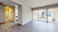 Located at 7000 Coachman Lane in Henrico, Virginia, this single-floor residence has been thoughtfully updated throughout, presenting a clean, modern aesthetic across all rooms. The main living area features durable luxury vinyl plank flooring in a neutral gray-wood tone, complemented by sliding glass doors that invite generous natural light and provide outdoor views of the surrounding wooded landscape. The space flows directly into a well-appointed galley-style kitchen, which showcases white shaker cabinetry with matte black hardware, light quartz countertops, a subway tile backsplash, and a full suite of stainless steel appliances including a gas range, built-in microwave, dishwasher, and refrigerator. A window at the end of the kitchen adds additional brightness to the space. The bedrooms are finished with plush carpeting and feature windows that frame views of the tree-lined surroundings. The bathrooms echo the kitchen's design language, offering white vanities topped with quartz, undermount sinks, matte black fixtures, and wood-look vinyl flooring. Neutral wall tones and consistent finishes throughout the unit create a cohesive and move-in ready environment.