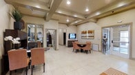 This single-floor space exudes a polished, professional atmosphere with a thoughtfully designed interior that balances functionality and comfort. The main area is anchored by a striking coffered ceiling with exposed beams, adding architectural depth and a sense of elegance to the open layout. Large neutral-toned floor tiles run throughout, enhancing the bright and airy feel of the space.

A central seating arrangement features a round table surrounded by upholstered chairs in warm blush tones, creating an inviting area well-suited for meetings or casual gatherings. A wall-mounted flat-screen television and a coordinating media console provide a functional focal point, complemented by a vibrant landscape painting that adds a natural, organic touch to the neutral palette.

The space includes multiple doorways leading to adjoining rooms, offering additional privacy and versatility. Decorative accents, including a suit of armor figurine and carefully placed artwork, lend the space a distinctive character. Recessed lighting integrated into the coffered ceiling ensures consistent, warm illumination throughout. Overall, the space presents a refined yet approachable environment, suitable for a variety of professional or communal purposes.