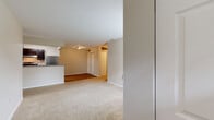 This single-floor residence offers a functional and well-organized layout designed for comfortable everyday living. The living area is generously sized, finished with neutral-toned wall-to-wall carpeting that lends a warm, cohesive feel throughout the space. A window near the front entry allows natural light to filter in, brightening the room alongside a transom window above the front door.

The kitchen is positioned adjacent to the living area and features a pass-through counter with granite-style surfaces, providing an open connection between the two spaces. Dark cabinetry pairs with stainless steel appliances, including a refrigerator and range, while wood-look flooring adds a clean, practical finish underfoot. A set of double doors in the kitchen area offers additional storage or pantry space.

The bedrooms are carpeted and neutrally painted, with one room featuring a window that provides views of surrounding greenery. Multiple closets are found throughout the unit, contributing to ample storage. The bathrooms each include a full soaking tub and shower combination with chrome fixtures, finished in clean white surrounds. Overall, the space presents a straightforward, move-in-ready layout with a calm, neutral palette throughout.