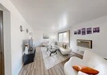 This single-floor residence offers a practical and well-organized layout across two bedrooms, one bathroom, a living room, dining room, and kitchen. Light-toned wood-style flooring runs throughout, creating visual continuity across all rooms.

The living room serves as the central gathering space, featuring crisp white walls, a large sliding window that draws in natural light and provides outdoor views, and a wall-mounted air conditioning unit. The open feel of the room makes it versatile and welcoming.

Adjacent to the living area, the dining room includes a ceiling fan and comfortably accommodates a dining table, making it functional for everyday use.

The kitchen is notably well-equipped, featuring dark shaker-style cabinetry extending to the ceiling for ample storage, granite-look countertops, a stainless steel sink, and black appliances including a refrigerator and range.

The primary bedroom is a generously proportioned room with a large window offering outdoor views, wood-style flooring, a sliding-door closet, and baseboard heating. The second bedroom mirrors similar finishes with a built-in closet.

The bathroom features a tiled tub-shower surround, a white vanity, and wood-style flooring, maintaining the clean aesthetic found throughout the residence.