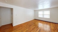 Located at 102 Manor Pkwy in Rochester, NY, this single-floor unit offers a straightforward and functional layout. The living area is a standout feature, showcasing warm, polished hardwood floors that run throughout, bright white walls, and a window that allows natural light to fill the space. A baseboard heating system provides consistent warmth, and the textured ceiling adds a subtle architectural detail. The additional room mirrors this aesthetic, with the same hardwood flooring, white walls, and a window fitted with blinds, creating a clean and adaptable space.

The kitchen is efficiently designed with ample white cabinetry extending to the upper walls for generous storage. A white electric coil range and a single-basin sink with a drain rack sit beneath the cabinetry, and a window with blinds brings in natural light. The tile flooring complements the bright, utilitarian feel of the space.

The bathroom features a tub and shower combination dressed in classic light blue wall tiles with brass fixtures, lending a retro character. A pedestal sink, toilet, and earthy tile flooring complete the room. Overall, this unit offers a clean, functional environment with classic details throughout.