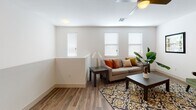 This two-story residence offers a well-designed layout with modern finishes throughout. The main living area features durable hardwood-style flooring and is bathed in natural light from multiple windows dressed with white blinds. A ceiling fan overhead adds comfort to the bright, open space. Adjacent to the living room, a dedicated dining area is highlighted by a sleek, multi-bulb linear pendant light, creating an inviting atmosphere for gatherings.

The kitchen is outfitted with stainless steel appliances, including an electric range and over-the-range microwave, complemented by light gray cabinetry, gray countertops, and a classic subway tile backsplash. A dedicated laundry room houses a full-size washer and dryer with overhead shelving for added storage.

The bedrooms feature plush carpeting, ceiling fans, and generous natural light from dual windows. The bathrooms are finished with gray countertops, undermount sinks, light wood cabinetry, large mirrors, and tiled tub-shower combinations with wood-style flooring. The overall aesthetic throughout the space is clean, contemporary, and functional.
