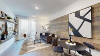 This single-floor residence showcases a thoughtfully designed interior that blends contemporary aesthetics with warm, natural textures. The open-concept living and dining area serves as the heart of the home, anchored by a dramatic reclaimed wood accent wall that spans the length of the living space. Built-in wooden shelving with integrated media storage lines one wall, adding both functionality and visual depth, while a sliding glass door floods the area with natural light and provides access to an outdoor balcony. Light wood-plank flooring runs throughout the main living areas, complementing the warm tones of the wood detailing.

The kitchen features light wood cabinetry, white quartz countertops, and a central island with bar seating. Stainless steel appliances, including a refrigerator, gas range, and microwave, are neatly integrated into the layout. Pendant lighting above the island adds a modern finishing touch.

The bedroom is a calm retreat with plush carpeting, generous natural light from a large window with elegant draping, and a walk-in closet. The bathroom continues the modern design language with a light wood vanity, white countertop, a full tub and shower with grey subway tile surround, and clean, minimalist finishes throughout. The overall ambiance is modern, cohesive, and inviting.