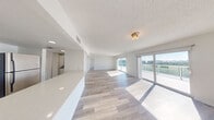 This single-floor residence is designed with a clean, modern aesthetic defined by a neutral white palette and light wood-style flooring that extends seamlessly throughout every room. The open-concept living and dining area is expansive, flooded with natural light streaming through large sliding glass doors that lead to a private balcony offering panoramic outdoor views of the surrounding landscape and skyline. The textured ceilings add a subtle architectural detail overhead.

The kitchen is thoughtfully positioned adjacent to the main living area, featuring white shaker-style cabinetry, a light quartz countertop that wraps into a breakfast bar, a tile backsplash, stainless steel appliances, and recessed lighting — providing both function and style.

The bedrooms are generously sized, each with walk-in or standard closets and access to natural light. One bedroom includes sliding glass doors that open directly to the balcony, reinforcing the connection to the outdoors. The bathroom offers a wide vanity with white cabinetry, a large mirror, a soaking tub and shower combination, and ample counter space. Overall, the space presents a bright, airy ambiance well-suited for comfortable everyday living.