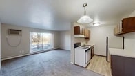 This single-floor unit offers a practical, straightforward layout that connects the living area and kitchen in an open arrangement. The living space is generously sized, finished with wall-to-wall carpet, and receives natural light through a large sliding glass door that opens to an outdoor balcony with views of surrounding trees. A wall-mounted air conditioning unit and baseboard heating provide year-round climate control in the living area.

The kitchen flows directly off the living space and is defined by warm-toned wood cabinetry that lines the upper and lower walls, offering ample storage. A gas range, refrigerator, and single-basin sink are included, alongside light wood-look vinyl flooring and a pendant light overhead. A countertop overhang provides additional prep space.

A dedicated bedroom offers carpeted flooring, neutral walls, and a closet with double doors, providing a quiet and private retreat. The bathroom includes a full-size soaking tub and shower combination, white square tile surround, a grab bar for accessibility, and a standard toilet. Textured ceilings are present throughout the unit, contributing to its classic residential character.