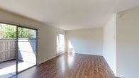 This single-floor unit is defined by a cohesive, open layout that seamlessly connects the living and kitchen areas. Rich, dark hardwood flooring runs throughout the space, lending warmth and continuity to each room.

The living area is generously proportioned, bathed in natural light from a large window and a sliding glass door that opens to an outdoor balcony or patio. The neutral, cream-toned walls complement the flooring and create a clean, versatile backdrop.

The kitchen is well-appointed and functional, featuring white shaker-style cabinetry with open display shelving, granite countertops in earthy tones, and a full suite of stainless steel appliances including a refrigerator, microwave, and electric range. A peninsula counter extends into the living space, defining the kitchen zone while maintaining the open-concept feel. Recessed lighting adds a polished touch overhead.

A corridor leads to the bathroom, which is finished with matching granite countertops, dark hardwood flooring, brushed nickel hardware, and towel bars. The space is clean and simply designed.

Overall, the unit offers a bright, well-connected interior with consistent finishes throughout, combining practical design with an inviting, comfortable ambiance.