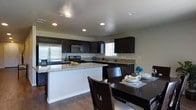 This single-floor residence offers a thoughtfully designed open-concept layout that seamlessly connects the kitchen and dining areas, creating an inviting and functional living environment. The kitchen is a standout feature, showcasing rich dark cabinetry that contrasts elegantly with light granite countertops. Stainless steel appliances, including a refrigerator, microwave, and gas range, provide a sleek, modern aesthetic. A kitchen peninsula extends the prep and serving space, making it ideal for both everyday cooking and entertaining. Recessed lighting throughout the kitchen and dining area ensures a bright and well-lit atmosphere, complemented by a window above the sink that brings in natural light. The adjacent dining space comfortably accommodates a dark wood dining table and chairs, echoing the rich tones found in the cabinetry. Warm hardwood flooring runs throughout, tying the spaces together with a cohesive and polished look. The neutral wall tones provide a versatile backdrop, allowing the dark wood and granite finishes to take center stage. Overall, this home combines practical design with refined finishes to create a comfortable and stylish living space.