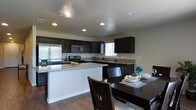 This single-floor residence offers a thoughtfully designed open-concept layout that seamlessly connects the kitchen and dining areas, creating an inviting and functional living environment. The kitchen is a standout feature, showcasing rich dark cabinetry that contrasts elegantly with light granite countertops. Stainless steel appliances, including a refrigerator, microwave, and gas range, provide a sleek, modern aesthetic. A kitchen peninsula extends the prep and serving space, making it ideal for both everyday cooking and entertaining. Recessed lighting throughout the kitchen and dining area ensures a bright and well-lit atmosphere, complemented by a window above the sink that brings in natural light. The adjacent dining space comfortably accommodates a dark wood dining table and chairs, echoing the rich tones found in the cabinetry. Warm hardwood flooring runs throughout, tying the spaces together with a cohesive and polished look. The neutral wall tones provide a versatile backdrop, allowing the dark wood and granite finishes to take center stage. Overall, this home combines practical design with refined finishes to create a comfortable and stylish living space.