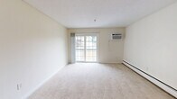 This well-laid-out two-bedroom, one-bathroom residence in Manchester, New Hampshire offers a comfortable and functional living experience across a single floor. The spacious living room features soft wall-to-wall carpeting, neutral cream-toned walls, and a sliding glass door that opens to a private balcony, allowing natural light to fill the space. A wall-mounted air conditioning unit and baseboard heating ensure year-round comfort.

The kitchen is equipped with rich, dark wood cabinetry, a tile backsplash, light stone countertops, and a full suite of black appliances including a refrigerator, electric range, and over-the-range microwave. Durable tile flooring runs throughout the kitchen and adjoining areas.

Both bedrooms are generously sized, featuring plush carpeting, baseboard heating, and ample natural light from large windows. The primary bedroom includes a mirrored sliding closet, offering practical storage. The second bedroom is versatile and well-proportioned.

The bathroom is clean and functional, featuring a full tub and shower combination with chrome fixtures, grab bars for added safety, and tile accents. The overall aesthetic throughout the unit is bright and neutral, creating a welcoming and move-in-ready environment.