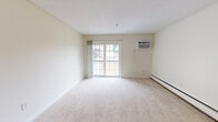 This well-laid-out two-bedroom, one-bathroom residence in Manchester, New Hampshire offers a comfortable and functional living experience across a single floor. The spacious living room features soft wall-to-wall carpeting, neutral cream-toned walls, and a sliding glass door that opens to a private balcony, allowing natural light to fill the space. A wall-mounted air conditioning unit and baseboard heating ensure year-round comfort.

The kitchen is equipped with rich, dark wood cabinetry, a tile backsplash, light stone countertops, and a full suite of black appliances including a refrigerator, electric range, and over-the-range microwave. Durable tile flooring runs throughout the kitchen and adjoining areas.

Both bedrooms are generously sized, featuring plush carpeting, baseboard heating, and ample natural light from large windows. The primary bedroom includes a mirrored sliding closet, offering practical storage. The second bedroom is versatile and well-proportioned.

The bathroom is clean and functional, featuring a full tub and shower combination with chrome fixtures, grab bars for added safety, and tile accents. The overall aesthetic throughout the unit is bright and neutral, creating a welcoming and move-in-ready environment.