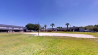 Located in Charleston, South Carolina, this outdoor community amenity space at Castlewood Townhomes offers residents a well-maintained recreational area designed for active outdoor enjoyment. The centerpiece of the space is a regulation-style sand volleyball court, complete with a net and poles, surrounded by a wide expanse of neatly kept green lawn that provides ample room for spectators and additional outdoor activities.

The setting is framed by mature palm trees and established landscaping, lending a distinctly Southern coastal character to the environment. The open-air layout takes full advantage of the abundant natural light typical of the Lowcountry region, with clear sightlines across the grounds. Residential buildings are visible in the background, situating the amenity comfortably within the broader community.

Lighting poles are positioned throughout the area, suggesting the space may be usable during evening hours. The combination of manicured turf, sandy court, and tropical greenery creates an inviting, resort-like atmosphere that encourages community interaction and recreational use. This amenity space reflects the outdoor-oriented lifestyle that Castlewood Townhomes offers its residents in the Charleston area.