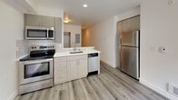 This thoughtfully designed studio unit offers a functional and modern single-floor layout that maximizes every square foot. The open-plan living and kitchen area serves as the heart of the unit, featuring light wood-style plank flooring that runs seamlessly throughout and lends a clean, contemporary feel.

The kitchen is well-appointed with a full suite of stainless steel appliances, including a refrigerator, range with oven, built-in microwave, and dishwasher. Light wood cabinetry pairs with white quartz-style countertops to create a bright, modern workspace, while the undermount sink adds a polished finishing touch.

The main living area is bright and open, benefiting from a large window with access to a private balcony, allowing for natural light and outdoor views. A track lighting fixture provides flexible overhead illumination.

A separate alcove or flex space features a sliding closet door, offering dedicated storage and the versatility to serve as a sleeping area. The bathroom is finished with matching light wood cabinetry, a white countertop vanity with a framed mirror, and the same cohesive wood-style flooring. The overall palette of whites, grays, and warm wood tones gives the unit a fresh, modern ambiance throughout.