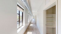 Located at 1107 S University Ave in the heart of Ann Arbor, this expansive 5-bedroom, 6-bathroom unit offers generous living space designed with a modern, urban aesthetic. The open-concept living room is bright and airy, featuring large floor-to-ceiling windows that flood the space with natural light and provide views of the surrounding cityscape. Exposed industrial-style ductwork adds a contemporary loft character, complemented by light wood-tone flooring and ceiling fans throughout. The well-appointed kitchen is a standout feature, centered around a large granite-topped island with bar seating, pendant lighting, stainless steel appliances, and rich dark wood cabinetry. Each of the five bedrooms offers a functional layout with carpeted flooring, individual windows, and access to one of six bathrooms. The bathrooms are consistently finished with warm wood vanities, granite countertops, light wood-look tile flooring, and walk-in glass shower enclosures. A spacious private terrace provides sweeping views of the surrounding Ann Arbor neighborhood and the University of Michigan campus. Two hallways connect the layout efficiently, making the overall flow practical for shared living. This unit combines modern finishes with industrial design elements in a prime location.