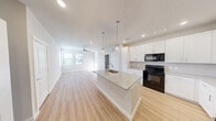 This well-appointed single-story home in Anacua offers three bedrooms and two bathrooms across a thoughtfully designed floor plan. The open-concept layout seamlessly connects the kitchen, dining, and living areas, creating a bright and cohesive main living space. Light wood-style flooring flows throughout the common areas, complemented by recessed lighting and ceiling fans that enhance the airy ambiance.

The kitchen serves as the centerpiece of the home, featuring a large central island with a granite countertop and undermount sink, pendant lighting, crisp white shaker cabinets with ample storage, and black appliances including a range, microwave, and refrigerator. The adjacent living area benefits from natural light through large windows and a ceiling fan overhead.

The primary bedroom is generously sized, offering a ceiling fan, closet access, and a comfortable sense of space. The additional bedrooms feature soft carpeting, ceiling fans, and windows that bring in natural light and outdoor views. The bathrooms are finished with granite-topped white vanities and wood-style flooring, maintaining a consistent, clean aesthetic throughout. A dedicated laundry area, multiple closets, and a hallway round out the functional layout of this move-in-ready home.