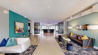 Located at 415 Stump Rd in Montgomeryville, PA, this single-floor amenity space is a vibrant, thoughtfully designed community hub. The welcoming lobby greets visitors with polished concrete floors, teal accent walls, patterned area rugs, and comfortable lounge seating — all bathed in natural light from large glass entry doors. Striking laser-cut decorative panels serve as architectural dividers throughout, adding visual interest and depth to the open layout.

The centerpiece of the space is the Luxor lounge — a dramatic circular bar finished in dark marble with gold-toned barstool bases, set beneath a sculptural tray ceiling with ambient purple lighting. A large-format display screen and warm wood-paneled walls complete the upscale atmosphere. Adjacent to the lounge, a dedicated beverage station labeled "Pour" offers convenient self-service amenities.

The game room features a full-size pool table, foosball table, high-top seating, and a sweeping large-scale abstract mural in vibrant teal, pink, and gold tones. Neon light installations add a contemporary artistic touch.

The fitness center is well-appointed with treadmills, cable machines, free weights, and weight benches spread across purple and grey carpet tiles. Ceiling fans, mirrored walls, and natural light from exterior windows make it a functional and energizing space. A motivational neon "beat yesterday" sign reinforces the athletic environment.