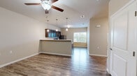 This single-story, 2-bedroom, 1-bathroom residence offers a functional and well-designed layout with a cohesive blend of modern finishes and comfortable living spaces. The open-concept kitchen and living area serves as the heart of the home, anchored by a peninsula breakfast bar illuminated by a trio of pendant lights. The kitchen is outfitted with rich, dark-stained wood cabinetry, light countertops, and stainless steel appliances, including a range and over-the-range microwave. Durable wood-look flooring runs throughout the main living area, complemented by a ceiling fan and vaulted ceilings that enhance the sense of openness. Natural light filters in through a window at the far end of the living space, adding brightness to the neutral, warm-toned walls. Both bedrooms feature plush wall-to-wall carpeting and neutral paint, creating a calm and restful atmosphere. The primary bedroom offers a comfortable footprint with a window bringing in natural light. The bathroom includes a clean, all-white walk-in shower stall with chrome fixtures. Throughout the residence, white baseboards and trim provide a crisp, finished look that ties each room together cohesively.