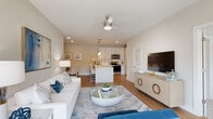 This thoughtfully designed single-floor residence offers a seamless open-concept layout connecting the living, dining, and kitchen areas. The living room is bathed in a neutral palette and features hardwood-style flooring, recessed lighting, a ceiling fan, and a large wall-mounted television. A bold blue abstract artwork anchors the space, complemented by a sliding glass door that invites natural light. The dining area accommodates a round glass-top table with elegant upholstered chairs, while a mirrored bar cabinet adds a sophisticated touch nearby.

The kitchen is equipped with crisp white shaker cabinetry, white quartz countertops, a classic subway tile backsplash, stainless steel appliances, a deep undermount sink, and pendant lighting — combining both style and functionality. A central island provides additional prep space and casual seating.

The primary bedroom features plush carpeting, a walk-in closet, and a private en-suite bathroom with a dual-sink vanity, white quartz countertops, and a tiled shower. A secondary bedroom is equally well-appointed with soft carpeting and natural light from a window with blinds. The secondary bathroom offers a clean, floating white vanity with a large mirror. A dedicated laundry area with a full-size washer and dryer adds everyday convenience throughout this well-appointed home.