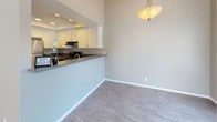 This single-floor residence offers a well-organized layout designed for comfortable everyday living. The open-concept kitchen is a functional highlight, featuring white cabinetry, dark countertops, a stainless steel refrigerator, and a gas range with an overhead microwave. A tray ceiling with recessed lighting adds architectural interest above the kitchen, which opens to the adjacent dining area via a peninsula counter. A pendant light fixture illuminates the dining space, which flows seamlessly onto light-toned wood-look flooring throughout the main living areas.

The living room is generously proportioned, anchored by a white brick fireplace and bathed in natural light through sliding glass doors that open to an outdoor area. Vaulted ceilings and a textured finish overhead add dimension to the space.

The bedrooms feature plush carpeting and vertical-blind windows that allow ample natural light. The neutral wall tones throughout create a calm, cohesive atmosphere. Two full bathrooms are finished with white vanities, dark countertops, wood-look tile flooring, and tub-shower combinations. A dedicated laundry area accommodates a full-sized washer and dryer, providing added convenience within the unit.