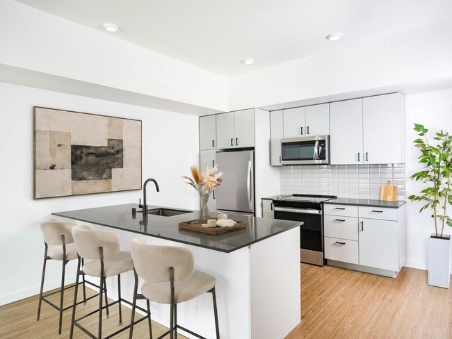 Kitchen with a spacious island, bar seating, and stainless steel appliances set within a bright layout designed for cooking and daily connection. - Modera Bridle Trails