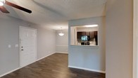 This single-floor residence offers a thoughtfully designed open layout that connects the living and dining areas seamlessly. Dark hardwood flooring runs throughout the main living spaces, providing a warm contrast to the soft, neutral gray walls and bright white baseboards and trim. A textured ceiling adds subtle character overhead, while a pendant light fixture anchors the dining area with a clean, understated elegance.

The kitchen is accessible via a pass-through window framed by a half-wall, offering both connectivity and definition between spaces. Inside, rich dark wood cabinetry pairs with light stone countertops and a classic tile backsplash, creating a balanced aesthetic. Black appliances complete the kitchen's cohesive look.

The overall ambiance of the space is calm and practical, with a clean, move-in-ready feel. The neutral tones and open sightlines allow natural light to circulate freely, making the space feel airy and welcoming. A white paneled door near the entry adds a crisp finishing detail. The single-floor layout ensures easy navigation and a comfortable flow between all areas of the home.