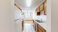 This 2-bedroom, 1-bathroom unit in Fargo, North Dakota offers a practical and functional layout across a single floor. The galley-style kitchen is well-equipped with warm oak cabinetry, a double stainless steel sink, electric range, dishwasher, and refrigerator, all set atop light ceramic tile flooring. Upper and lower cabinet storage runs the length of both walls, providing ample space for kitchen essentials. The kitchen opens directly into a combined dining and living area, where light hardwood-style flooring transitions to carpet. Natural light filters through vertical-blind-covered windows, and a ceiling fan adds comfort to the space. A wall-mounted air conditioning unit is also present in the living area. Both bedrooms feature plush carpet, baseboard heating, natural window light, and full-panel bifold closet doors offering generous storage. The unit includes four closets in total, ensuring plenty of storage throughout. The full bathroom is clean and straightforward, featuring a tub-shower combo with tile surround and tile flooring. A utility room rounds out the layout, adding practical functionality. The textured ceilings and warm wood trim details are consistent throughout, giving the unit a cohesive, understated character.