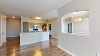 This single-floor residence offers a thoughtfully designed open-concept layout that seamlessly connects the kitchen, dining, and living areas. Rich hardwood-style flooring flows throughout the main living spaces, complemented by crisp crown molding and clean white trim that add a polished architectural touch. The living area is bright and airy, featuring large windows that invite natural light and a ceiling fan overhead, while arched doorways and decorative columns lend elegant structural character to the space.

The kitchen is well-equipped with stainless steel appliances, including a range with microwave above and a refrigerator, set against a classic white subway tile backsplash. Gray cabinetry with arched door detailing provides generous storage, and a peninsula with stone-look countertops offers additional workspace and casual seating potential.

The bedrooms are carpeted for comfort, with neutral tones and natural light from multiple windows. One room features built-in shelving and a dedicated desk area, making it ideal for use as a home office or study. The bathroom is clean and functional, finished with wood-look vinyl flooring, a tiled soaking tub and shower combination, and coordinating cabinetry with stone countertops. Throughout the home, a cohesive neutral palette and consistent finishes create a calm, inviting atmosphere.
