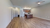 This well-appointed single-floor residence offers a thoughtfully designed open-concept layout that seamlessly connects the kitchen, dining, and living areas. The kitchen is a standout feature, showcasing rich walnut-toned cabinetry with sleek hardware, a white subway tile backsplash, quartz countertops, and a central island with an integrated sink — ideal for both meal preparation and casual dining. Stainless steel appliances, including a refrigerator, range, and microwave, complete the modern kitchen ensemble. Pendant lighting above the island and recessed ceiling lights provide both task and ambient illumination throughout.

The open living area is anchored by warm hardwood-style flooring that extends throughout the main living spaces, complemented by a ceiling fan and large French doors that flood the room with natural light and open to a private balcony. Transom windows above the doors enhance the sense of openness and airiness.

The bedrooms feature plush carpeting, neutral wall tones, and generous proportions, offering a quiet and comfortable retreat. A well-configured bathroom includes a soaking tub with shower, a vanity with walnut cabinetry, and direct access to an in-unit stacked washer and dryer along with a dedicated closet space — delivering exceptional functionality within a clean, contemporary aesthetic.