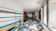 Located at 4470 S Lemay Ave in Fort Collins, Colorado, this fitness center delivers a comprehensive workout environment within a single, well-organized floor. The space features a bold, energetic design highlighted by a striking geometric-patterned floor in blue, gray, and white tones, paired with white walls adorned with wide blue horizontal stripes. Recessed lighting throughout the textured ceiling ensures the space is well-lit, while large windows along multiple walls allow natural light to fill the room and offer views of the surrounding outdoor area, including a glimpse of a pool.

The exercise room is thoughtfully divided into functional zones. A dedicated turf area hosts a bold red functional training rig complete with suspension trainers, a heavy punching bag, agility rings, and a weight bench, supporting strength and high-intensity training. The cardio zone features Matrix treadmills, an elliptical machine, and stationary cycling bikes. Additional equipment includes cable machines, a weight rack with medicine balls and stability balls in various sizes, and a tanning bed tucked into an adjoining hallway room. A wall-mounted flat-screen TV and an inspirational wall decal reading "The Best Project You'll Ever Work On Is You" add to the motivating atmosphere of this well-appointed fitness facility.