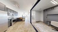 Located at 2750 Griffin Rd in Dania Beach, FL, this modern 2-bedroom, 1-bathroom unit offers a thoughtfully designed open-concept layout across a single floor. The kitchen is a standout feature, showcasing dark gray cabinetry, stainless steel appliances, a striking gold apron-front sink, dark stone countertops, and a peninsula with seating for multiple bar stools — ideal for both cooking and entertaining. A geometric LED light fixture adds a contemporary focal point overhead. The flooring throughout features a warm, marbled epoxy finish that flows seamlessly from the kitchen into the living area. The living room is bright and airy, benefiting from large sliding glass doors that open to a private balcony with open views of the surrounding landscape. The primary bedroom is a calm, light-filled retreat with a built-in closet, while the second bedroom features a large window with scenic outdoor views. One bedroom is configured with a built-in murphy-style desk and floor-to-ceiling gray cabinetry, offering versatile use as a home office. The bathroom is sleek and minimalist, featuring a glass-enclosed shower, a marble-top vanity with black fixtures, and an illuminated mirror. The overall ambiance is clean, modern, and refined.