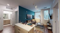 This well-designed single-floor residence offers a thoughtful layout with modern finishes and a cohesive contemporary aesthetic. The open-concept kitchen flows seamlessly into the living and dining area, creating an efficient and social space. The kitchen is equipped with stainless steel appliances, including a refrigerator, range, and microwave, complemented by white upper cabinetry, warm wood-toned lower cabinets, and a kitchen island with a white quartz countertop that doubles as a dining surface. Rich wood-look flooring runs throughout the main living area, adding warmth to the space. The living room is defined by a bold teal accent wall, track lighting on the ceiling, and large windows that invite abundant natural light. Multiple bedrooms provide comfortable personal retreats, each featuring carpet flooring, generous windows with blinds, and closet storage. The bathrooms are finished with wood-toned vanities, white quartz countertops, large mirrors, and wood-look flooring. One bathroom includes a glass-enclosed walk-in shower, while the other offers a clean, functional layout. A bold red entry door adds a distinctive design touch at the front entrance, setting the tone for the modern and vibrant interior throughout.