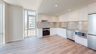 Located on the 10th floor at 492 W 41st Ave in Vancouver's Cambie corridor, this well-appointed 2-bedroom, 2-bathroom unit offers a bright and modern living experience across a thoughtfully designed single-level layout. Light wood-look flooring flows throughout, complementing the neutral palette of crisp white walls and clean trim work.

The kitchen is a standout feature, showcasing floor-to-ceiling windows that flood the space with natural light and frame open city views. Sleek white cabinetry with under-cabinet lighting, a marble-style tile backsplash, stone countertops, and a full suite of stainless steel appliances — including a refrigerator, built-in microwave, dishwasher, and range — make this a highly functional space.

The primary bedroom benefits from expansive floor-to-ceiling glazing, offering sweeping views of the surrounding Vancouver skyline and mountains beyond. The second bedroom is well-proportioned with its own window and access to natural light. Both bedrooms are serviced by their own dedicated bathrooms — one featuring a soaking tub with modern chrome fixtures and full-height white tile surround, and the other a clean, minimalist design with a floating vanity and large mirror. A dedicated closet and balcony round out this refined urban residence.