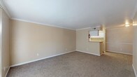 This two-story residence offers a practical and comfortable layout across two well-defined levels, connected by a carpeted staircase. The main level features a generously sized living area finished with warm beige walls, plush carpet flooring, and elegant crown molding that frames the space. A pass-through kitchen counter opens directly to the living area, providing a functional connection between the two spaces. White cabinetry and overhead ventilation are visible in the kitchen, lending a clean, organized aesthetic.

The upper level hosts a spacious bedroom retreat complete with a ceiling fan and light fixture, a closet, and direct access to a full en-suite bathroom. The bathroom features a single-sink vanity with a light countertop, white cabinetry with storage drawers, a large mirror, and a combined shower and bathtub with hardwood-style flooring.

An additional carpeted bedroom on the lower level offers crown molding, a chair rail detail along the walls, and a ceiling-mounted light fixture, providing a well-finished and cozy feel. Throughout the residence, consistent warm neutral tones, white trim, and carpeted floors create a cohesive and inviting atmosphere. The upper bedroom benefits from natural light through a window with blinds, adding brightness to the space.