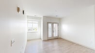 This single-floor unit presents a clean, contemporary design characterized by bright white walls, light wood-look flooring in the main living areas, and an open layout that promotes a sense of spaciousness. The living area is a notable highlight, featuring a large window alongside a set of French doors fitted with blinds that welcome abundant natural light and provide outdoor views, lending the space an airy, welcoming atmosphere.

The kitchen is well-appointed with light wood-tone flat-front cabinetry, white quartz-style countertops, a tile backsplash, and a full suite of stainless steel appliances including a refrigerator, range, built-in microwave, and dishwasher. Recessed lighting overhead adds a polished finish to the space.

The bedrooms feature plush neutral carpeting and windows that bring in natural light, creating comfortable, quiet retreats. The bathroom is finished with wood-grain cabinetry accented by matte black hardware, a white countertop, brushed gold light fixtures, and a full tub-shower combination with a curved rod.

A dedicated in-unit laundry area with a full-size washer and dryer adds everyday convenience. Throughout the unit, the consistent use of light tones and modern finishes creates a cohesive, move-in-ready environment.
