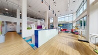 Located at 617 S Wright St in Champaign, Illinois, this single-floor amenity space serves as the community hub for Smile Fairlawn Student Living. The design is bold and contemporary, characterized by soaring double-height ceilings, expansive floor-to-ceiling windows, and an abundance of natural light that floods the interior throughout the day.

At the heart of the space is a striking reception desk finished in vibrant blue and frosted glass panels, anchored by a geometric wall installation that adds a strong visual focal point. The flooring transitions between warm wood-tone planks and colorful hexagonal carpet tiles in blue, gray, and teal, guiding movement through distinct functional zones.

The lounge area features bright magenta and patterned seating positioned against large glazed walls overlooking the streetscape. A micro market with refrigerated units and a bold mural of flamingos provides a lively casual zone. Collaborative open workspaces offer green ergonomic chairs and long shared tables beneath dramatic magenta acoustic ceiling panels.

Glass-walled, reservable study rooms provide quieter, focused environments equipped with wall-mounted displays and modular furniture. Throughout the space, curated artwork, tropical plants, and carefully considered lighting contribute to an energetic yet functional atmosphere designed for student life.