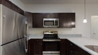 This single-floor residence is designed with a cohesive, modern aesthetic throughout. The kitchen serves as a focal point, outfitted with rich dark-espresso cabinetry, speckled granite countertops, and a full suite of stainless steel appliances including a refrigerator, electric range, and over-the-range microwave. Wood-style flooring runs through the kitchen, which opens to the living area via a peninsula with pendant lighting overhead — an ideal setup for casual dining or entertaining.

The living area is generously proportioned, featuring neutral carpet, white walls, and a wall-mounted split HVAC unit. The open sightlines between the kitchen and living space create a connected, functional layout. Bedrooms are carpeted and bright, each equipped with ceiling fans and windows with blinds. One bedroom features a walk-in closet, while the primary bedroom connects directly to an en-suite bathroom.

The primary bathroom includes a granite-topped vanity with dark cabinetry, a large mirror, and a glass-enclosed walk-in shower. A second bathroom mirrors the design aesthetic with matching granite and dark cabinetry, complemented by a full tub-shower combination and wood-style flooring throughout.