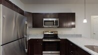 This single-floor residence is designed with a cohesive, modern aesthetic throughout. The kitchen serves as a focal point, outfitted with rich dark-espresso cabinetry, speckled granite countertops, and a full suite of stainless steel appliances including a refrigerator, electric range, and over-the-range microwave. Wood-style flooring runs through the kitchen, which opens to the living area via a peninsula with pendant lighting overhead — an ideal setup for casual dining or entertaining.

The living area is generously proportioned, featuring neutral carpet, white walls, and a wall-mounted split HVAC unit. The open sightlines between the kitchen and living space create a connected, functional layout. Bedrooms are carpeted and bright, each equipped with ceiling fans and windows with blinds. One bedroom features a walk-in closet, while the primary bedroom connects directly to an en-suite bathroom.

The primary bathroom includes a granite-topped vanity with dark cabinetry, a large mirror, and a glass-enclosed walk-in shower. A second bathroom mirrors the design aesthetic with matching granite and dark cabinetry, complemented by a full tub-shower combination and wood-style flooring throughout.