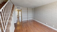 This two-story residence showcases a cohesive design centered around painted brick accent walls that appear throughout, lending a warm, textural character to nearly every room. The main living area on the first floor features gleaming hardwood flooring and a striking wall of built-in white shelving, ideal for display or storage. A carpeted staircase connects the two levels, continuing the space's blend of materials and finishes.

The kitchen is thoughtfully outfitted with white cabinetry, a stone-look tile backsplash, stainless steel appliances including a gas range, refrigerator, and dishwasher, pendant lighting, and hardwood floors. A sliding glass door with vertical blinds allows natural light to pour in.

Upstairs, the bedrooms continue the painted brick accent wall motif and are finished with plush carpeting. Each room features a ceiling fan with light fixture, and one room opens to a sliding glass door, adding natural light and ventilation. The bathrooms include a full bath with a tub-shower combination and hardwood flooring, as well as a half bath with a granite-style vanity countertop. Textured ceilings are present throughout, completing the space's consistent and functional aesthetic.