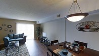 Located at 301 Barcelona Dr in Fayetteville, NC, this two-story home offers a practical and comfortable layout designed for everyday living. The main level showcases an open-concept living and dining area seamlessly connected by rich hardwood flooring that runs throughout. The dining area is highlighted by a pendant light fixture overhead and offers ample space for a full dining set, making it ideal for both casual meals and entertaining. Adjacent to the dining space, the living area benefits from a large sliding glass door dressed with vertical blinds, inviting an abundance of natural light and providing access to the outdoors. A textured ceiling adds a classic touch to the space, while neutral wall tones create a versatile backdrop adaptable to a variety of interior styles. The living area comfortably accommodates a seating arrangement and media setup, with generous floor space enhanced by a decorative area rug. Lush indoor greenery adds a welcoming, lived-in character to the room. Spread across two floors, this home provides well-defined living spaces that balance openness on the main level with the privacy and functionality of additional rooms above, making it a well-rounded residence in the Fayetteville community.
