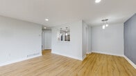 This thoughtfully renovated single-floor residence showcases a clean, contemporary design throughout. The open-concept living and dining area is finished with light-toned hardwood flooring and recessed lighting, creating a bright and airy atmosphere. A wall of floor-to-ceiling sliding glass doors leads to a private balcony, flooding the space with natural light and offering views of the surrounding greenery and cityscape beyond.

The kitchen features a pass-through window that connects seamlessly to the living area, stainless steel appliances including a gas range and built-in microwave, white cabinetry, light quartz countertops, and a striking teal herringbone tile backsplash that serves as a bold design focal point. Pendant lighting adds a refined finishing touch.

The bedrooms are carpeted for comfort and bathed in natural light from large windows dressed with vertical blinds. Generous closet space is provided, with at least one bedroom featuring a double-door closet. One bedroom is accented with a distinctive blue-purple feature wall, adding character to the space.

The bathroom is finished with large-format tile flooring, a white vanity with mirror, and brushed nickel fixtures, offering a clean and functional design. Throughout, the neutral color palette and modern finishes create a cohesive, move-in-ready living environment.