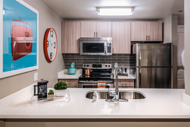 Cocina del apartamento con electrodomésticos de acero inoxidable, encimeras de cuarzo y suelos de madera. - Griffis Belltown