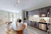 This thoughtfully designed one-bedroom, one-bathroom residence in Medford, MA offers a efficient and modern living experience across a single floor. The open-concept layout seamlessly connects the kitchen, dining, and living areas, creating a bright and functional shared space. The kitchen is outfitted with sleek dark wood cabinetry, white countertops, a cooktop, stainless steel wall oven, dishwasher, and refrigerator, all illuminated by under-cabinet and track lighting. A rounded wood dining table sits at the center of the combined living and dining area, which benefits from large floor-to-ceiling windows that flood the space with natural light and provide views of the surrounding greenery. The bedroom is a comfortable retreat featuring hardwood-style flooring, a double closet, and its own set of large windows with outdoor views. The bathroom is clean and functional, finished with light tile flooring, a wood-toned vanity, and accessibility-friendly grab bars. Two closets provide ample storage throughout the unit, and a dedicated laundry area adds everyday convenience. The overall aesthetic is contemporary and cohesive, with neutral tones and modern finishes throughout.