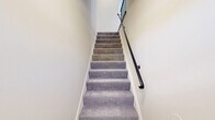 Located at 6660 Sanzo Rd in Pikesville, MD, this two-floor residence offers a thoughtfully laid-out living space spread across two levels. The main upper floor hosts the majority of the living areas, including a generously sized bedroom with soft carpet flooring, a large window that invites natural light and outdoor views, and direct access to a dedicated walk-in closet complete with built-in shelving and hanging rods for ample storage. The full bathroom features clean white tile flooring, a glass-enclosed shower, a white vanity, and a window that provides natural ventilation and light. The kitchen is well-appointed with rich dark cabinetry in a shaker style, light marble-look countertops, a gas range, dishwasher, refrigerator, and durable hardwood-style flooring — a practical and stylish space for everyday cooking. A hallway connects the main living areas with ease. A staircase leads down to a compact lower level, which opens into a bright, carpeted open room featuring recessed lighting and a window — ideal as a flex or bonus space. Neutral warm tones and cream-colored walls throughout lend the space a clean, cohesive ambiance, while consistent finishes across floors provide a unified aesthetic.