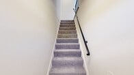 Located at 6660 Sanzo Rd in Pikesville, MD, this two-floor residence offers a thoughtfully laid-out living space spread across two levels. The main upper floor hosts the majority of the living areas, including a generously sized bedroom with soft carpet flooring, a large window that invites natural light and outdoor views, and direct access to a dedicated walk-in closet complete with built-in shelving and hanging rods for ample storage. The full bathroom features clean white tile flooring, a glass-enclosed shower, a white vanity, and a window that provides natural ventilation and light. The kitchen is well-appointed with rich dark cabinetry in a shaker style, light marble-look countertops, a gas range, dishwasher, refrigerator, and durable hardwood-style flooring — a practical and stylish space for everyday cooking. A hallway connects the main living areas with ease. A staircase leads down to a compact lower level, which opens into a bright, carpeted open room featuring recessed lighting and a window — ideal as a flex or bonus space. Neutral warm tones and cream-colored walls throughout lend the space a clean, cohesive ambiance, while consistent finishes across floors provide a unified aesthetic.