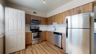 This single-floor residence offers a thoughtfully designed layout that balances functionality and comfort throughout its living spaces. The kitchen stands out with warm wood-toned cabinetry extending to the upper walls, a full suite of stainless steel appliances including a refrigerator, range, microwave, and dishwasher, complemented by a clean white tile backsplash and light hardwood-style flooring. The open living and dining area is generously proportioned, featuring neutral-toned carpet, a pendant light fixture, and an abundance of natural light streaming through large windows fitted with vertical blinds and a sliding glass door that opens to the outdoors. The bedrooms continue the carpeted, neutral aesthetic, each offering natural light through windows with horizontal blinds, providing a calm and adaptable space. The bathrooms are finished with light tile flooring and neutral walls. The primary bathroom includes a long dark-toned vanity with a white countertop, a wide mirror, and brushed nickel fixtures, while a secondary bathroom features a dark vanity and a bi-fold closet door. The overall ambiance of the space is clean, bright, and move-in ready, offering a welcoming environment with a consistent, modern design palette throughout.