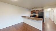 Located at 2865 W Elliott Dr in Spokane, WA, this single-floor, three-bedroom, two-bathroom unit offers a functional and comfortable layout across a well-utilized footprint. The open-concept kitchen is a standout feature, equipped with rich dark wood cabinetry, black appliances including a refrigerator, range, and built-in microwave, a double-basin sink, and a peninsula breakfast bar that flows seamlessly into the living area. Durable hardwood-style flooring runs throughout the kitchen and main living spaces, adding warmth and easy maintenance. The two bathrooms are clean and practical — one features a tub-shower combination with hardwood-style floors and a vanity with ample storage, while the second offers a similarly appointed design with well-lit vanity mirror. Each of the three bedrooms is carpeted in a neutral tone, offering a cozy feel, and the primary bedroom provides a comfortable, private retreat. Secondary bedrooms feature large windows with vertical blinds, allowing natural light to fill the rooms while providing views of the surrounding neighborhood. Baseboard heaters in the bedrooms ensure consistent warmth throughout the colder months. A hallway and dedicated closet provide additional storage and connectivity throughout the unit.