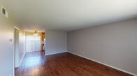 Located at 10233 Mission Gorge in Santee, this single-floor unit offers a practical and comfortable layout with consistent finishes throughout. The living area is spacious and open, showcasing rich, dark hardwood-style flooring that runs throughout the main living space. Neutral gray walls provide a clean backdrop, while a large window fitted with vertical blinds allows natural light to fill the room. A wall-mounted HVAC unit ensures year-round climate control, and a ceiling fan adds additional comfort.

The kitchen is well-appointed with warm oak cabinetry extending from floor to ceiling, offering generous storage. Granite-style countertops provide a durable workspace, complemented by a double-basin sink, a stainless steel refrigerator, and matching appliances. Recessed lighting and a window keep the space bright and functional.

The bedrooms are carpeted for comfort, each featuring ceiling fans and mirrored sliding closet doors that enhance the sense of space. One bedroom includes built-in shelving within the closet for added organization. The bathroom is neatly finished with a wood vanity topped with a granite-style surface, a full tub-shower combination, and hardwood-style flooring, completing this well-maintained unit.